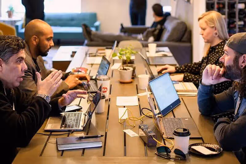 a group of people sitting at a table with laptops