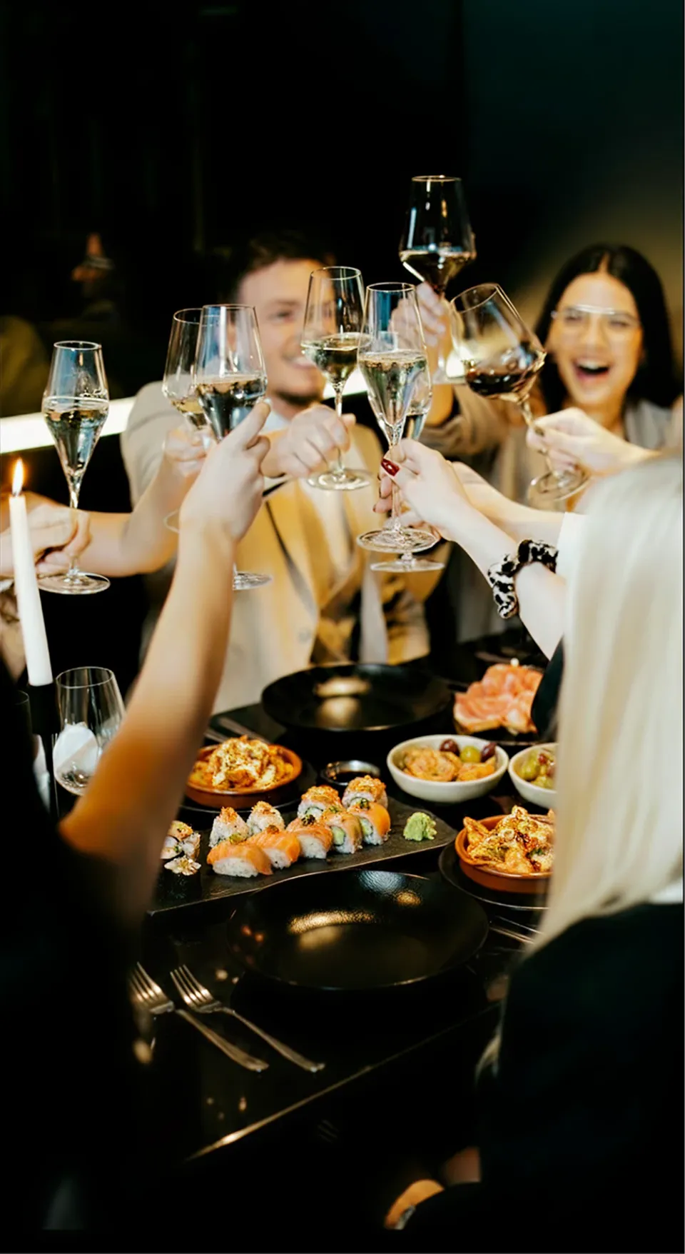 People dining together using utensils to eat food from plates with drinks on a wooden table.