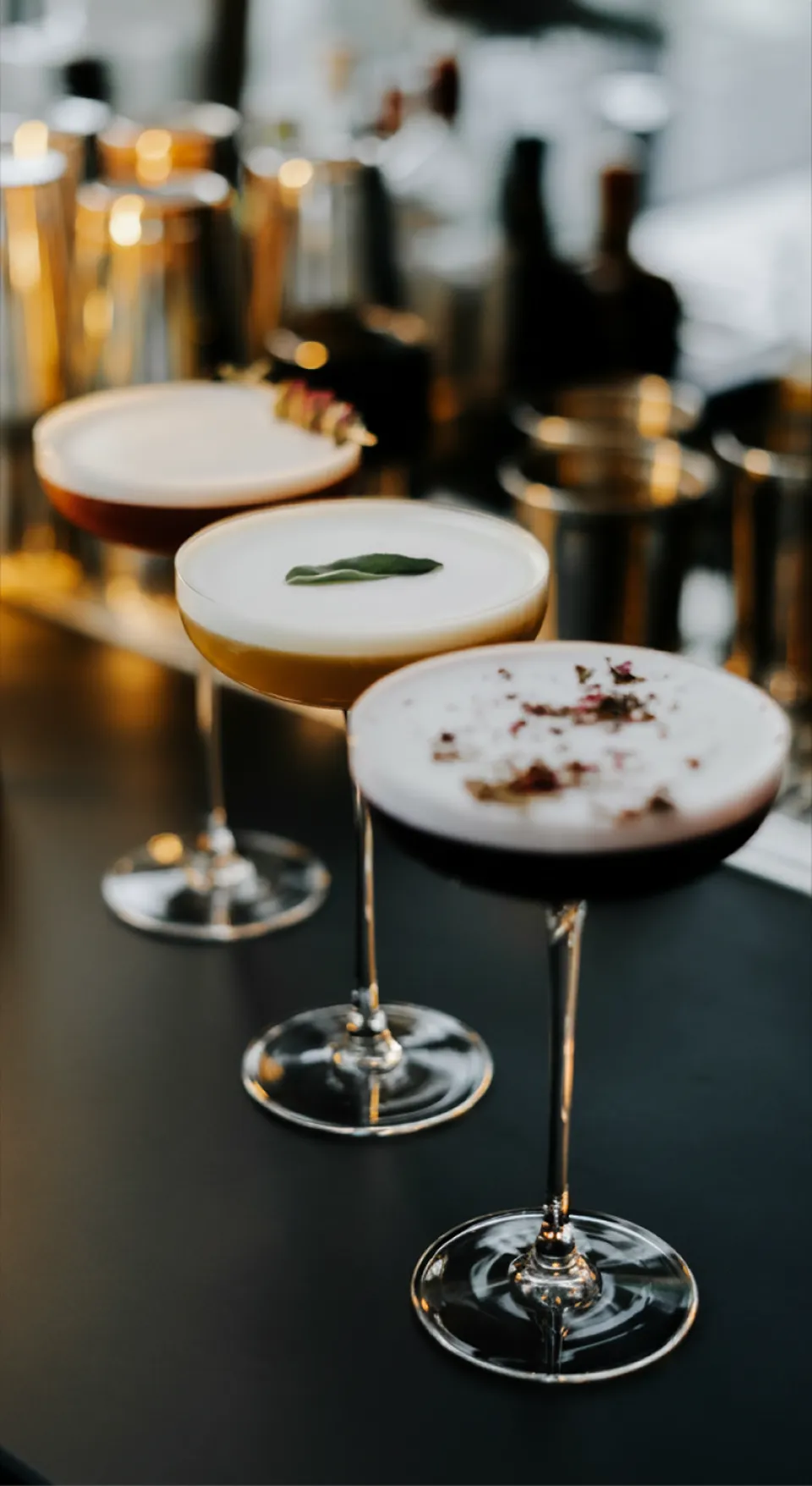 A glass of orange cocktail with a mint garnish and straw on a wooden table at sunset.