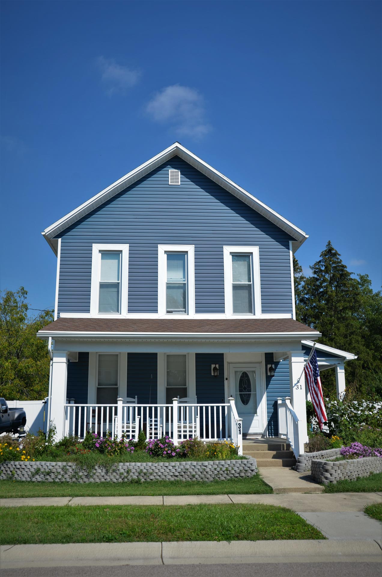 Street view of a blue house with white trim and an American flag flying from the front porch
