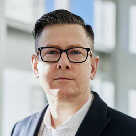 Portrait of a middle aged caucasian man with dark hair and wearing black framed glasses