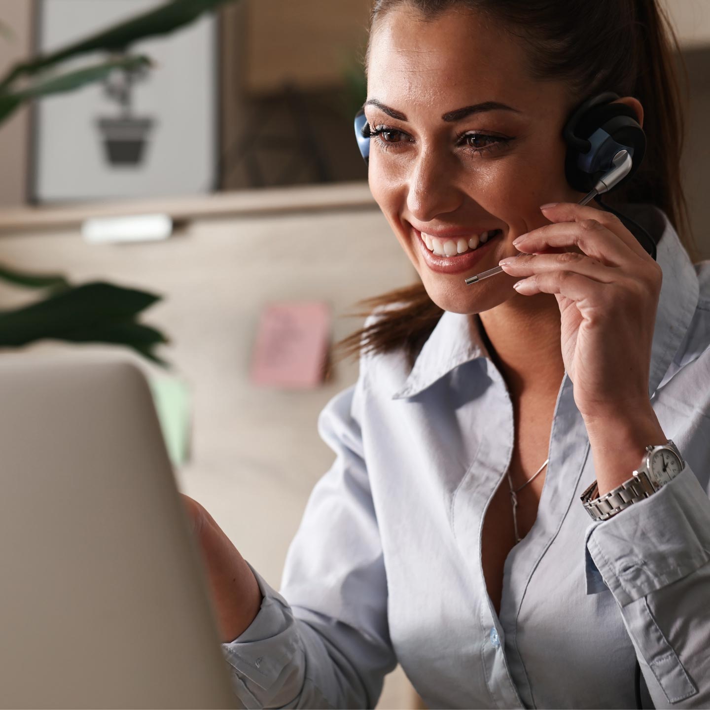 A brunette white woman sitting at a  computer and talking on her headset