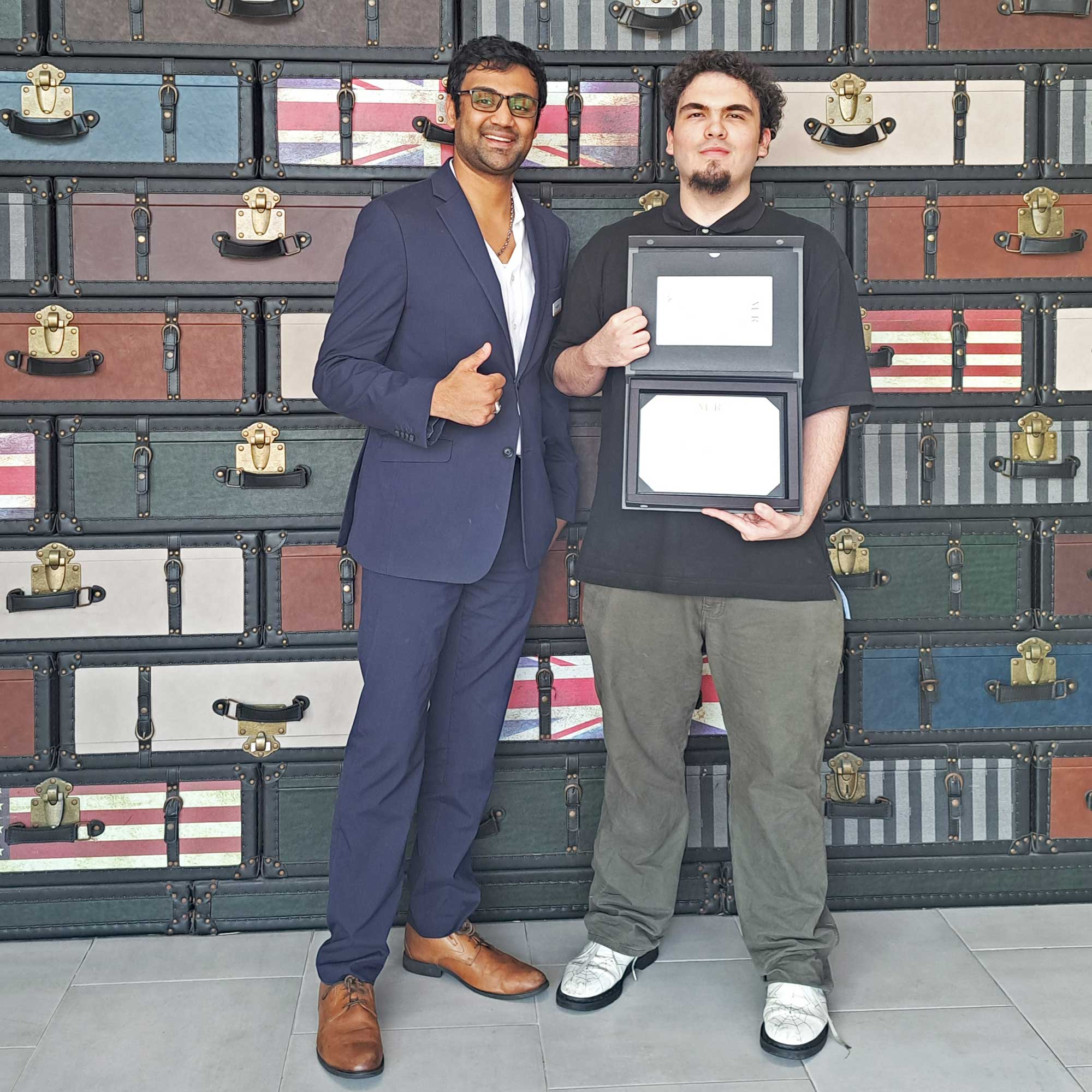 Assistant General Manager Samil Parikh presents Guest Service Agent Alexander Marquez with his one-year anniversary plaque at the Comfort Inn JFK Airport.
