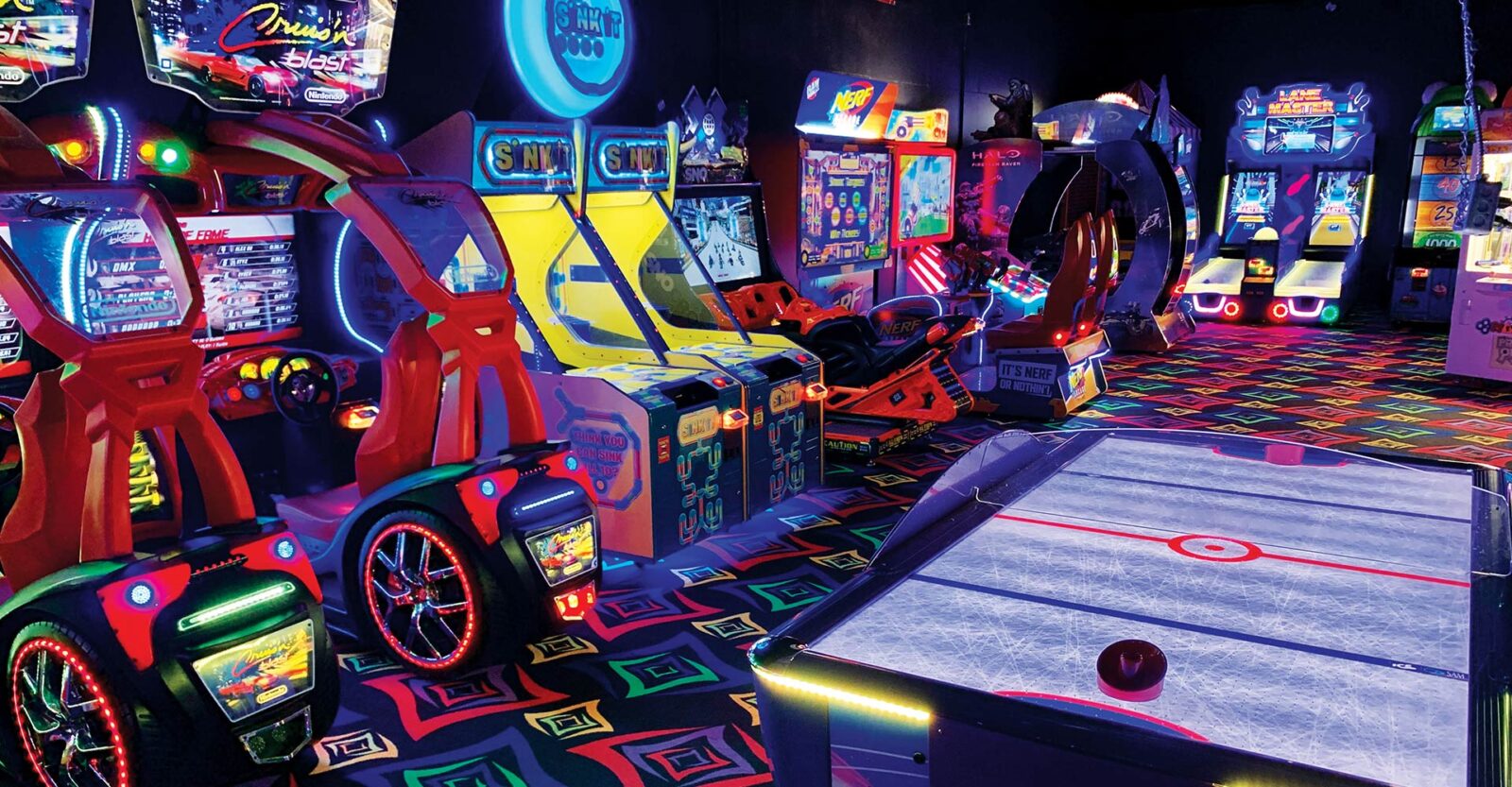 A bowling alley with a neon lit up car and a pool table.