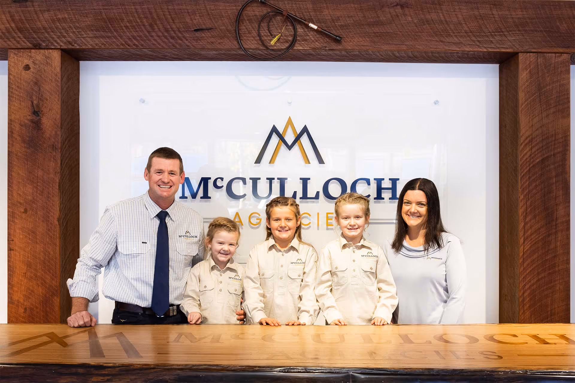 A smiling family of five standing in front of McCulloch Agencies logo