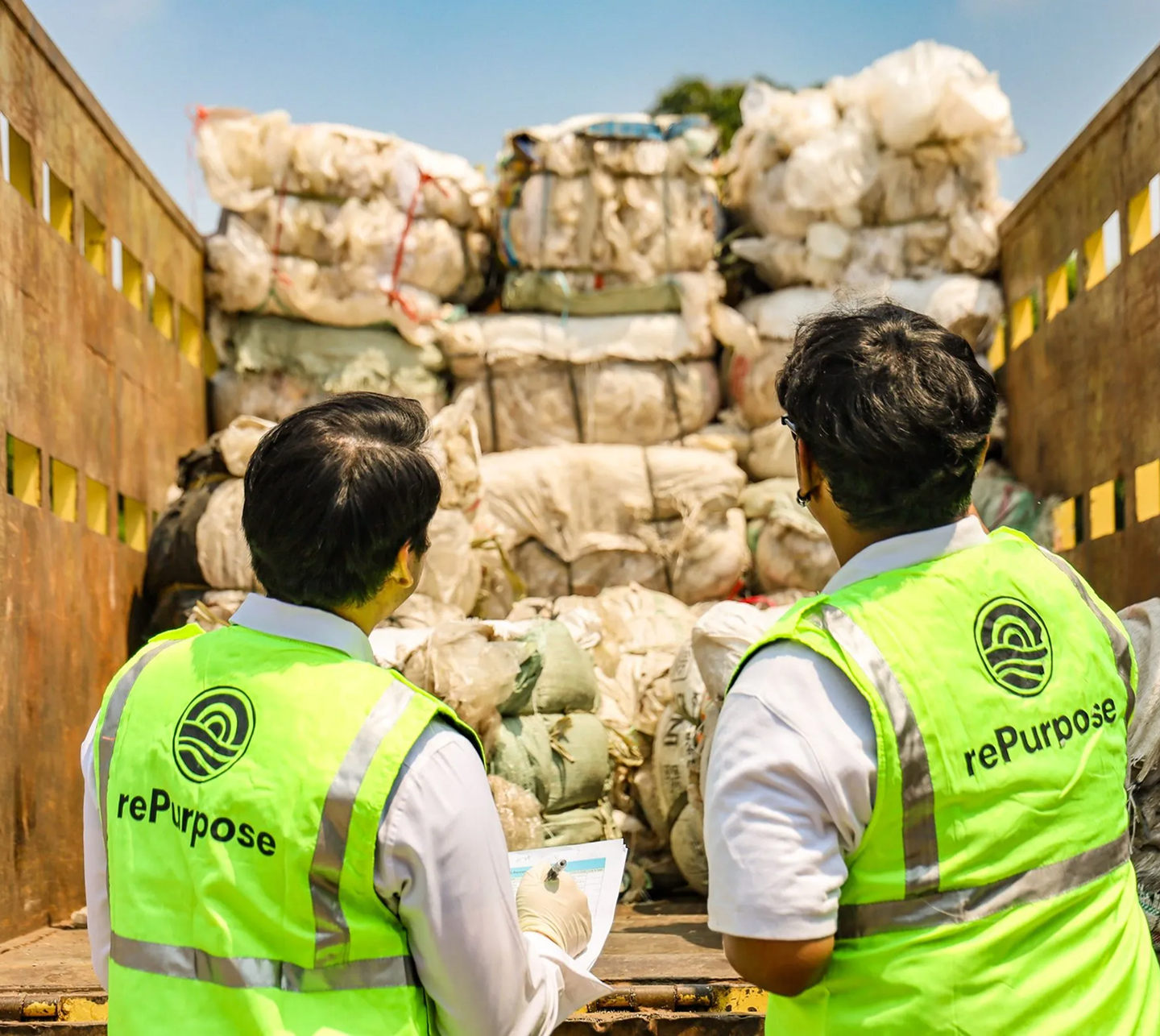 two men in reflective vests looking at a truck full of bags