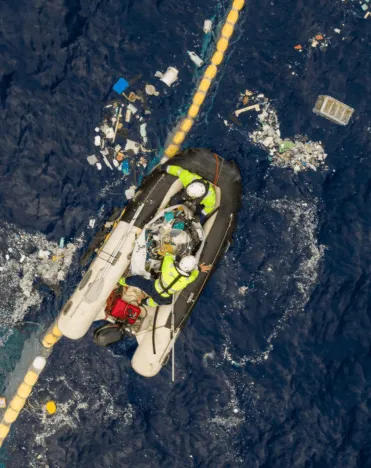 Two men in a boat pick up trash from the sea
