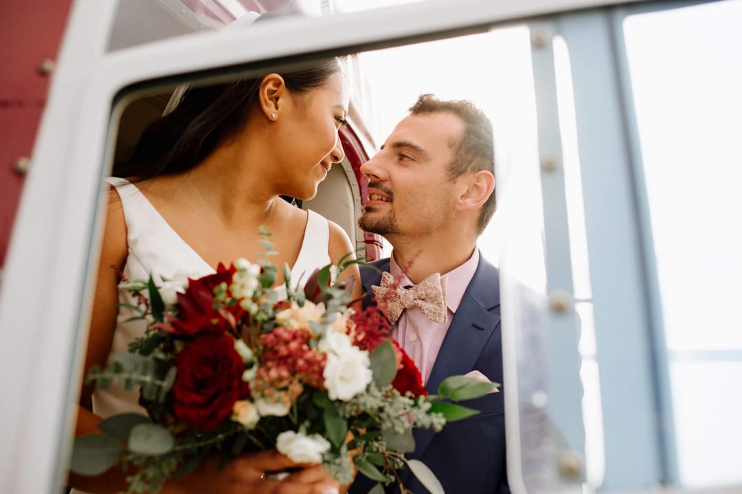 A couple gaze into eachother's eyes while in wedding outfits. They are on a helicopter.