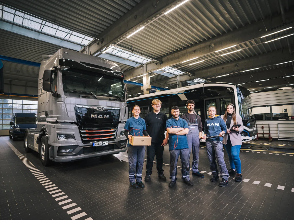 Team von MAN Truck & Bus vor einem Lkw und einem Bus in der Werkstatthalle