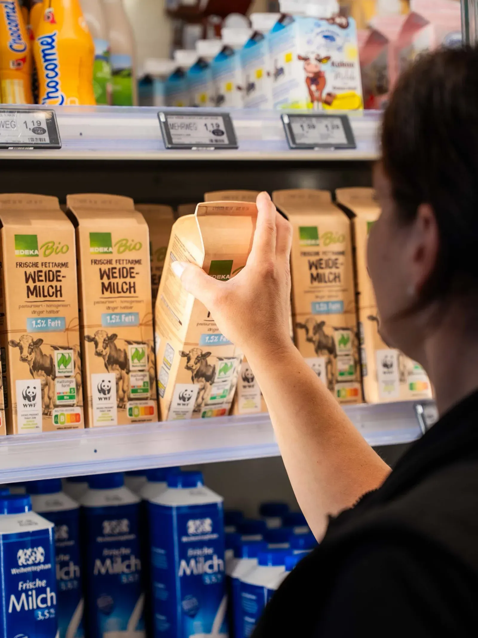Hand greift nach einer Milchpackung im Regal