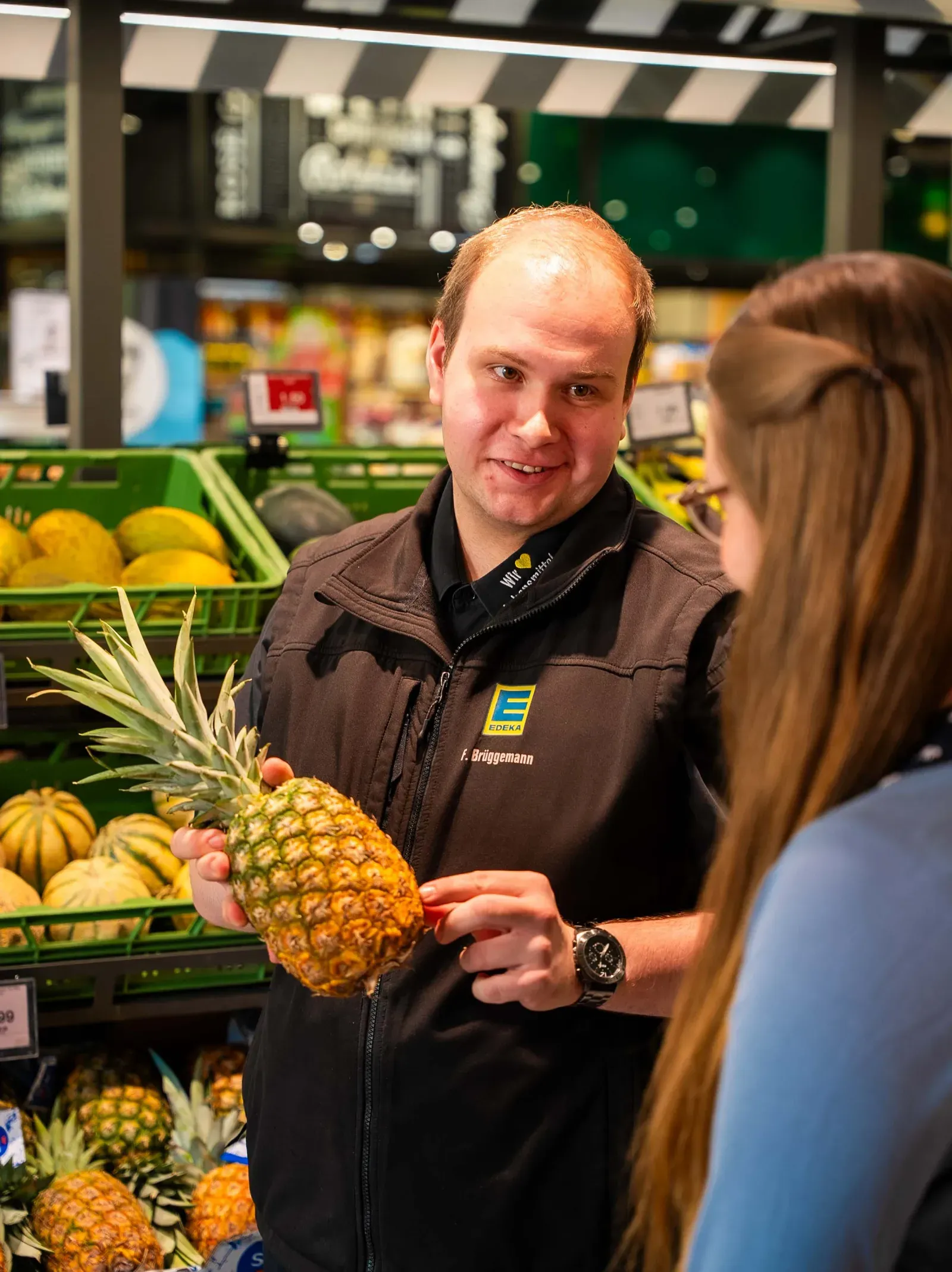 Mitarbeiter zeigt einer Kundin eine Ananas