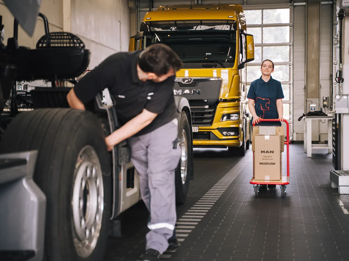 Mechatroniker am Rad einer MAN Zugmaschine, im Hintergrund ein MAN Lkw