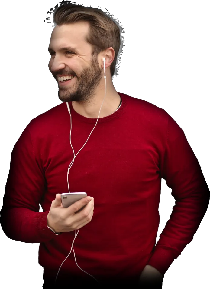 Smiling man in a red sweater listening to music with white earphones and holding a smartphone.