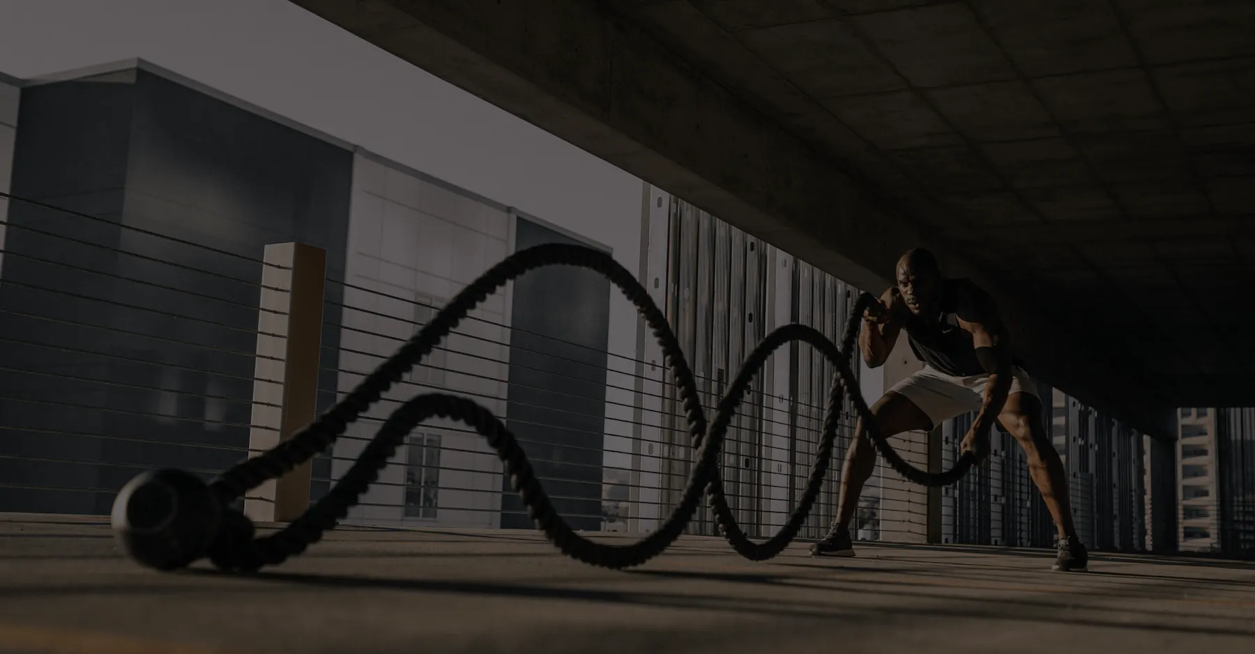 Athlete performing battle rope exercise under an urban concrete overpass.