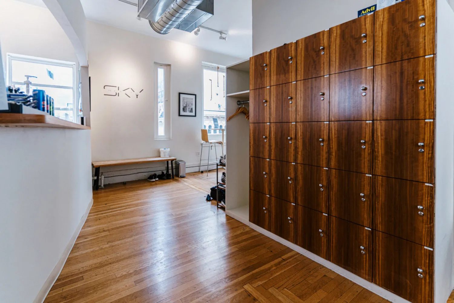 Interior of a room with wooden lockers on the right, a bench under two windows, and a logo reading 'SKY' on the wall.