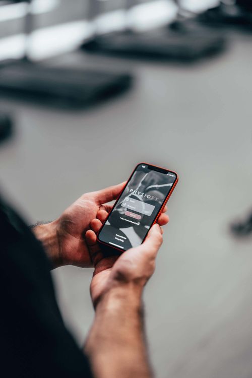 Person holding a smartphone displaying the PHYSIORX app login screen with email and password fields.