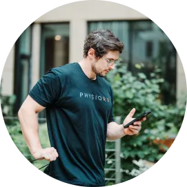 Man wearing a black PHYSIORX t-shirt looking at his smartphone outdoors near greenery.