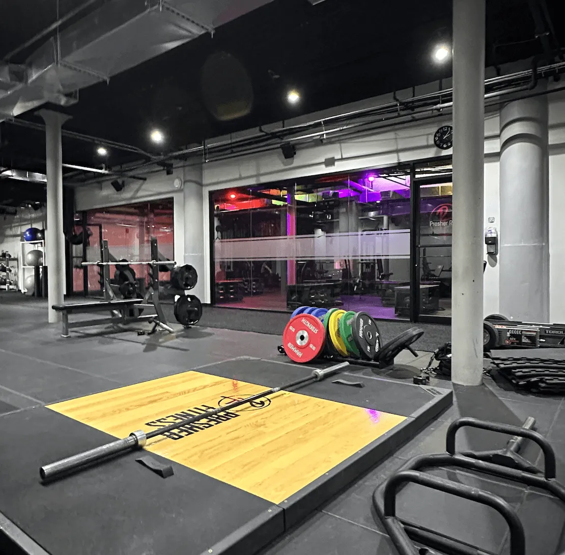 Indoor gym area with weightlifting platform, barbell, colorful weight plates, and bench press station.