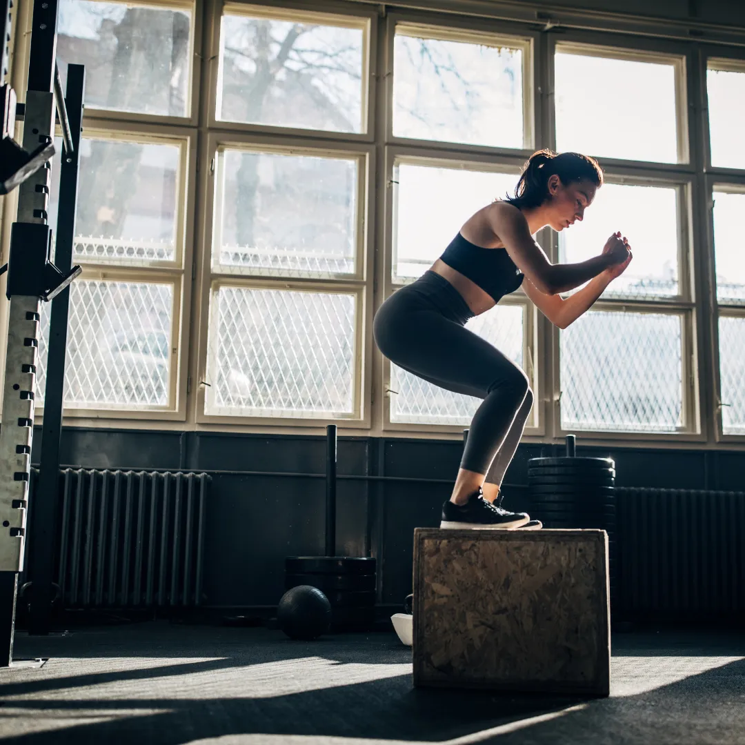 Woman stepping up onto a wooden plyometric box in a sunlit gym