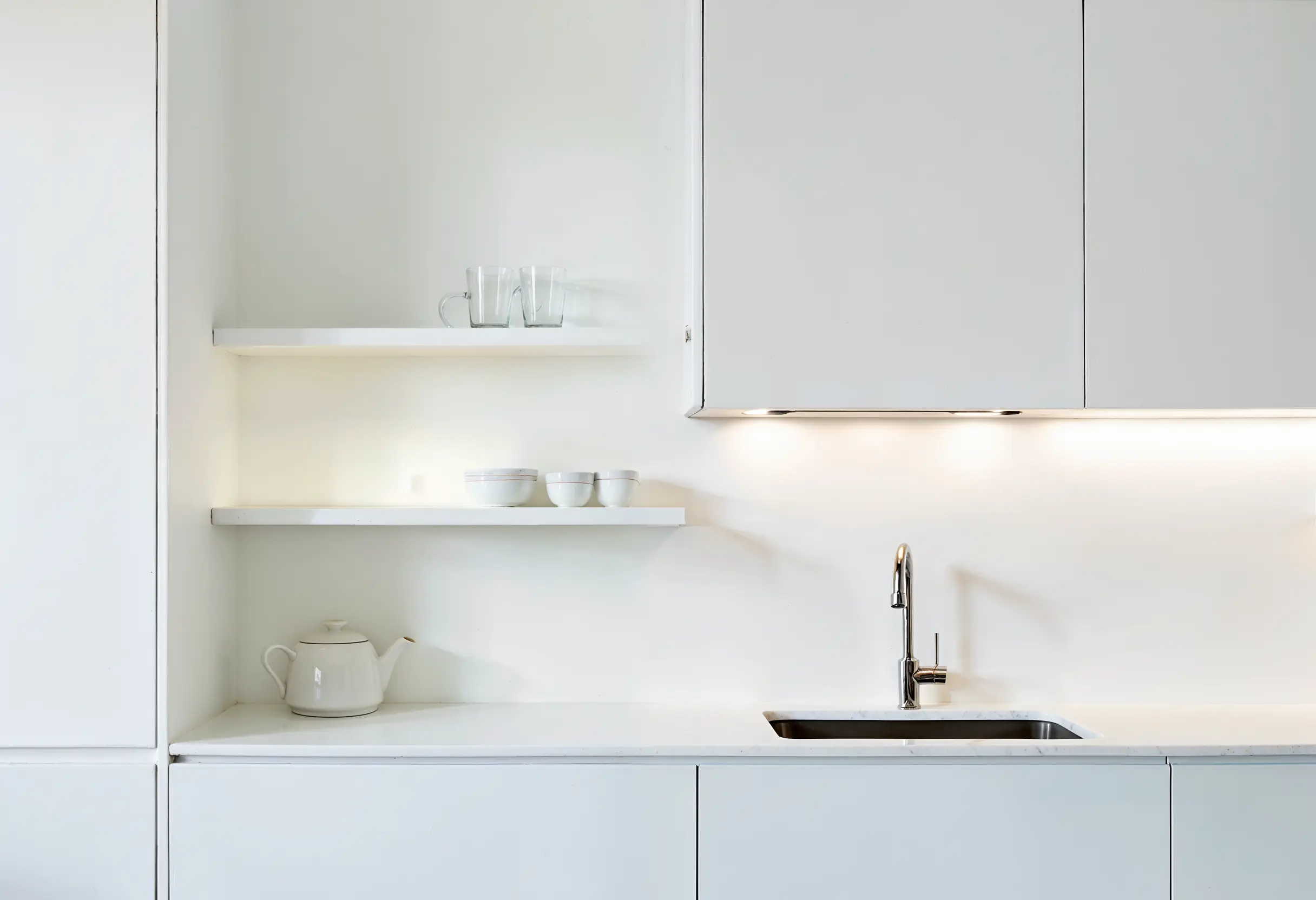 Minimalist white kitchen with floating shelves, soft lighting, and neatly arranged essentials