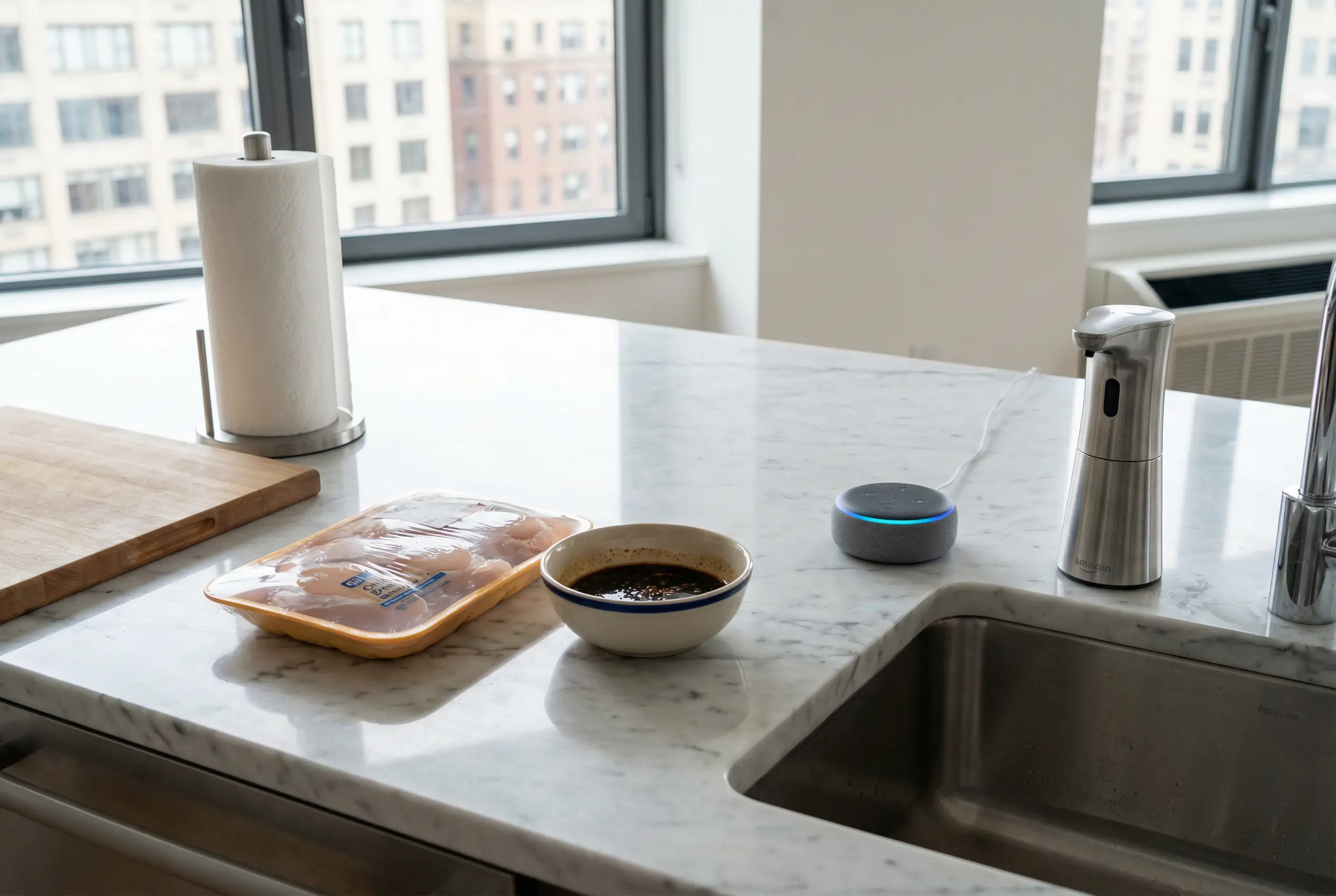 Voice assistant on a kitchen island next to raw chicken prep items in a Manhattan kitchen, showing hands-free hygiene.