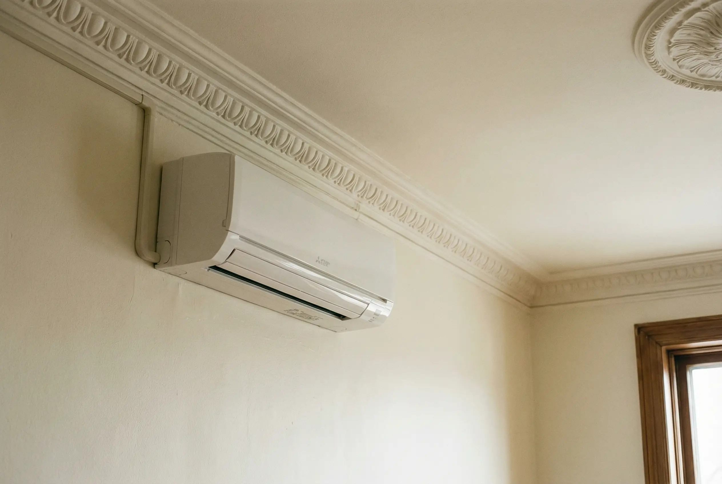 Ductless mini-split HVAC unit professionally installed in pre-war Manhattan apartment below ornate crown molding with minimal wall penetration
