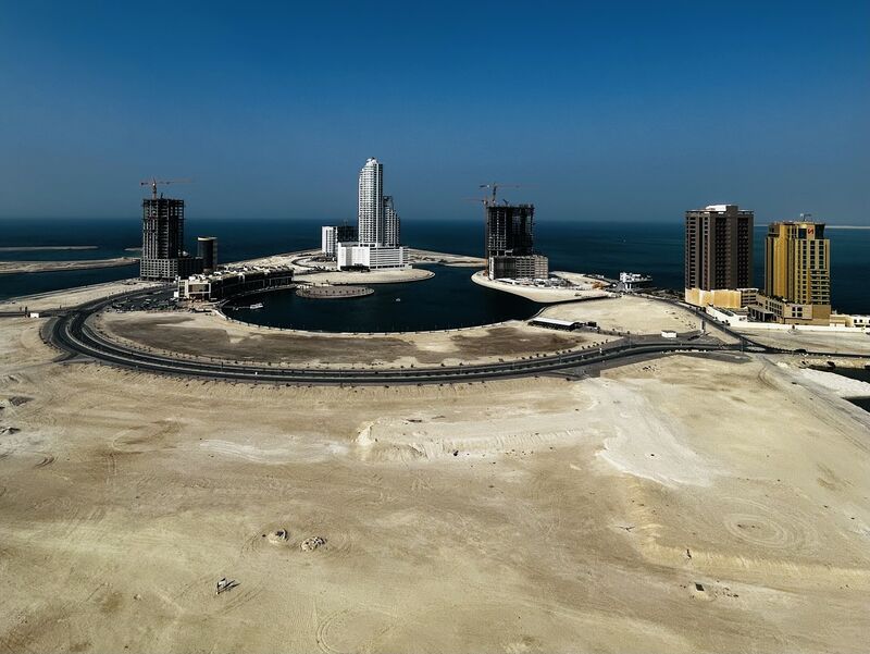 Coastal construction in Bahrain, with high-rises and cranes surrounding a man-made lagoon amid a wide desert landscape.