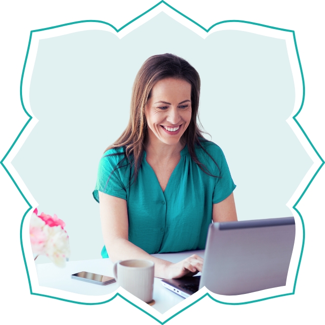 Eine lächelnde Frau sitzt am Schreibtisch und arbeitet an ihrem Laptop.
