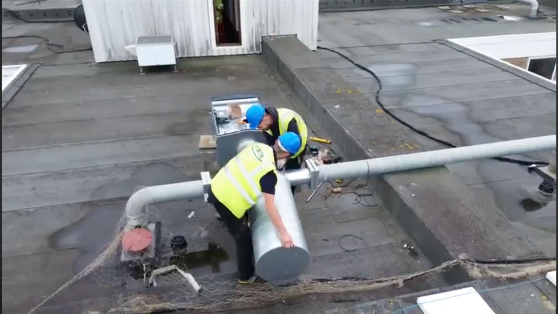 2 men in high vis jackets fitting a ventilation system on a roof