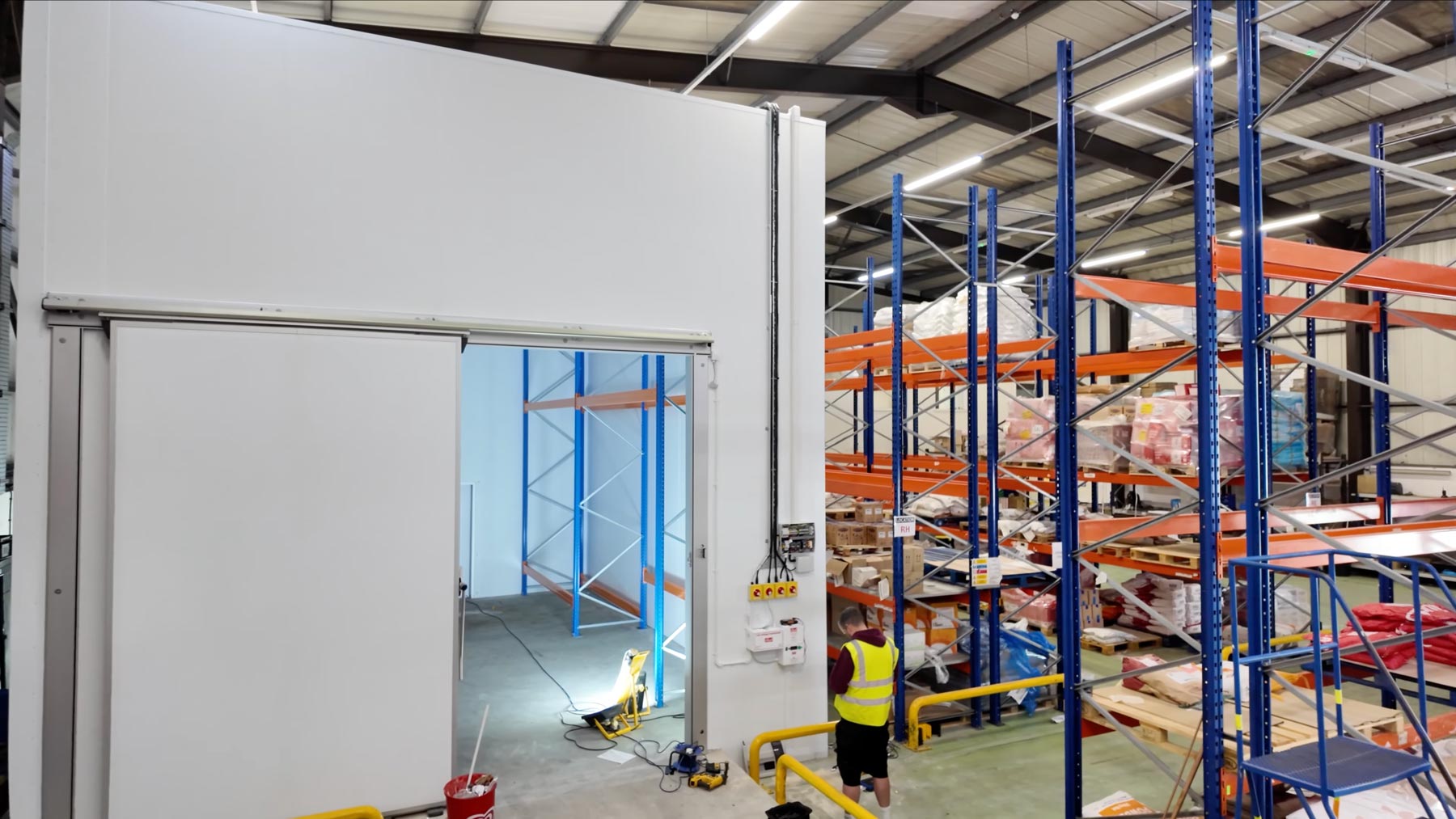 A wide shot of a large commercial freezer unit inside a large warehouse with racking