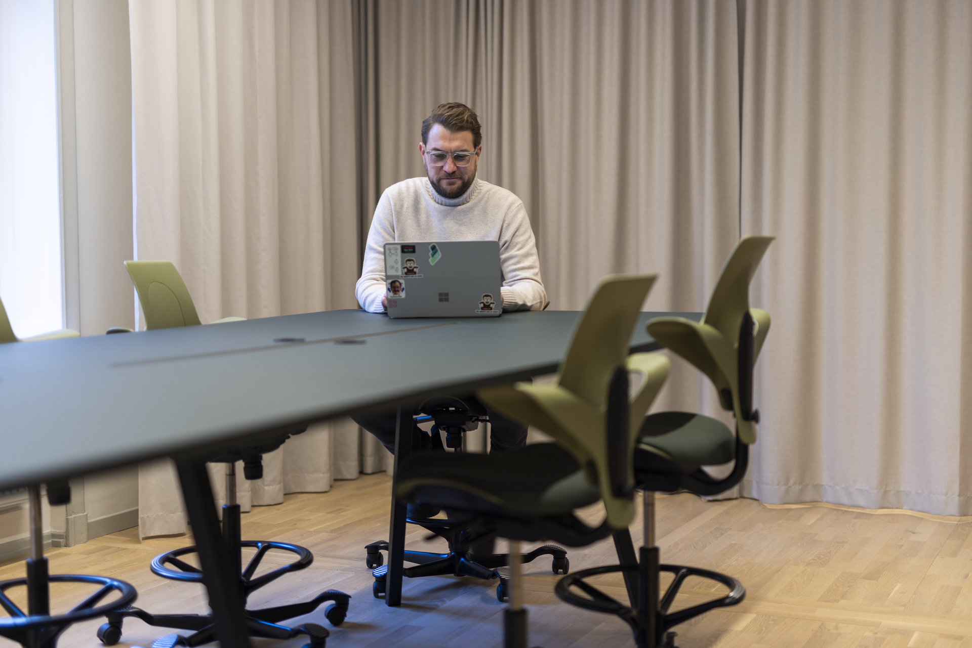 Risto Lavett, CEO at Redeploy is sitting with his computer, with stickers on it, on a long table.