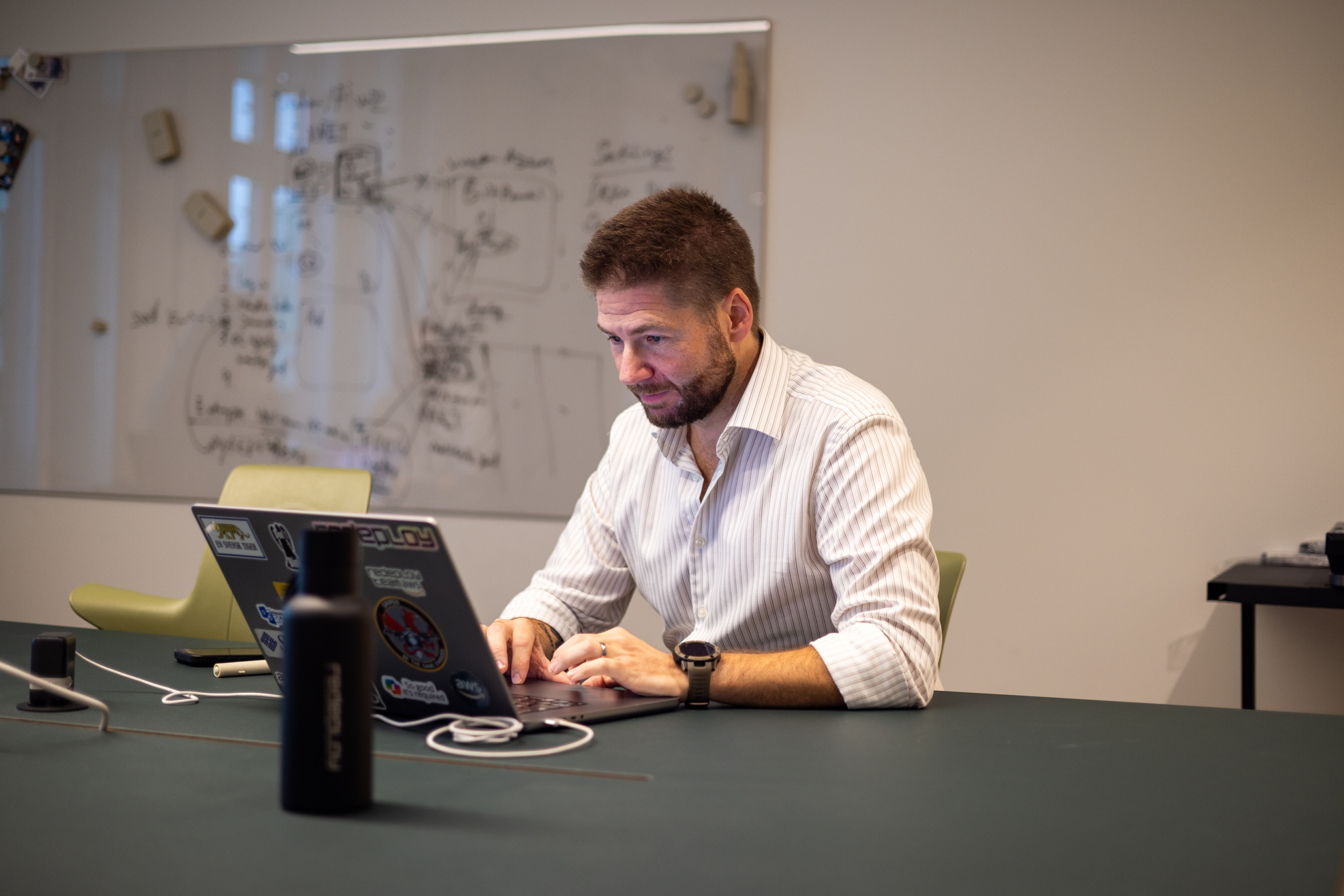 Lars Hasselrot working at his laptop in a meeting room at the Stockholm office, with an architecture sketch on the whiteboard behind him.