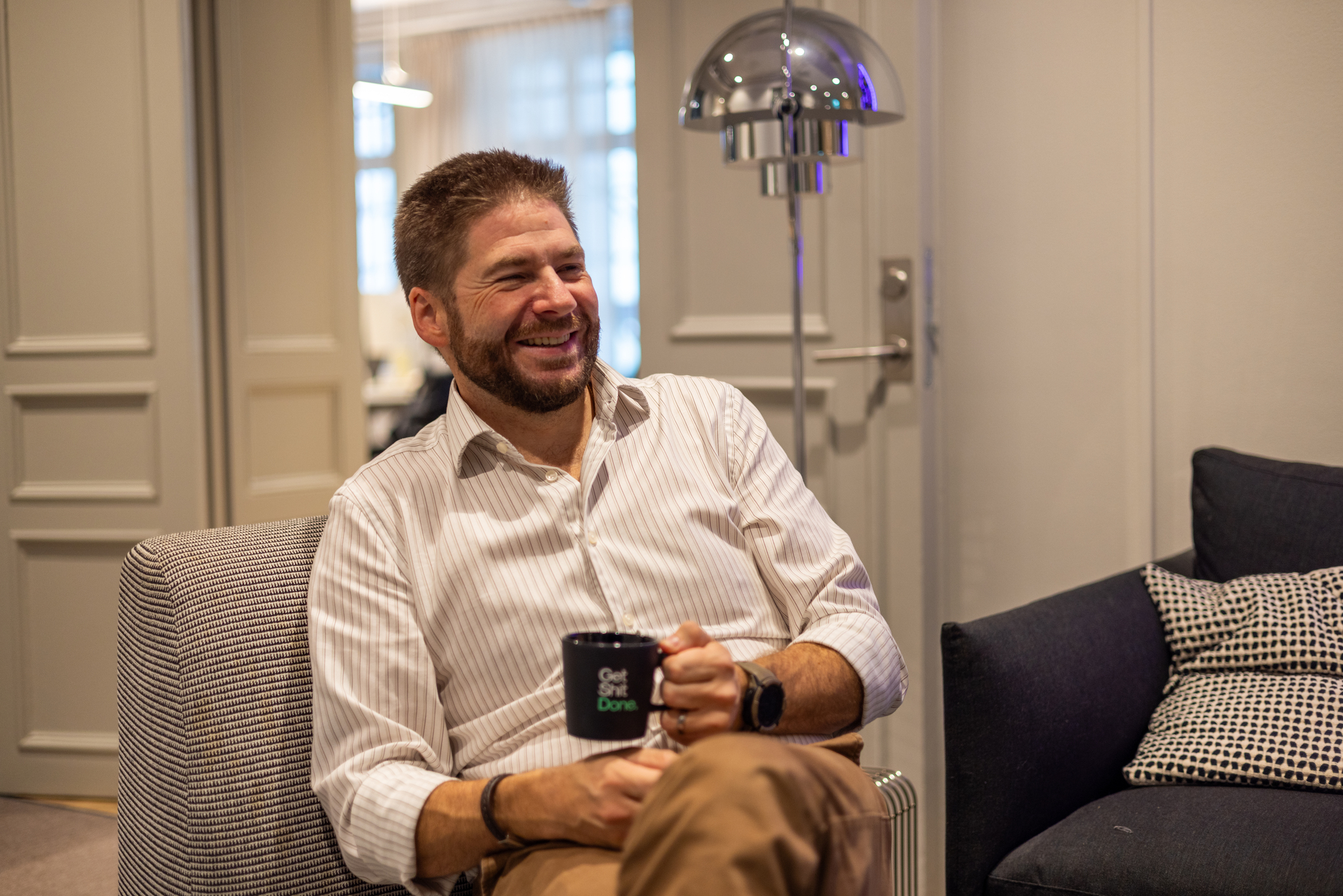 Lars Hasselrot laughing in an armchair at the Redeploy office, holding a coffee mug
