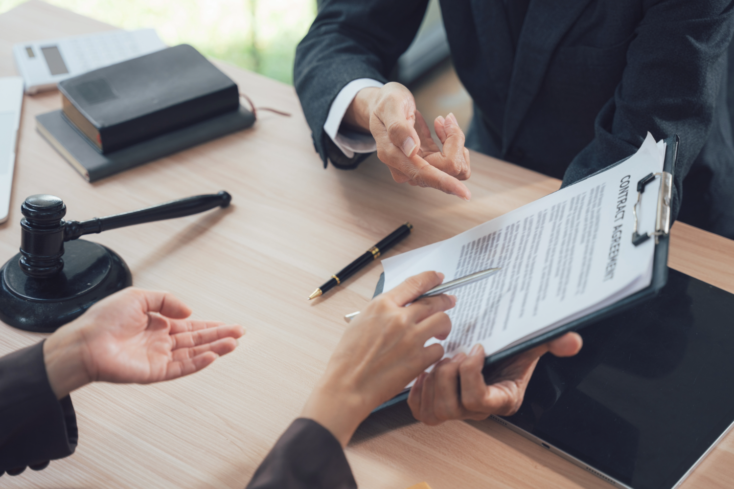 Two businesspeople discussing a contract with a legal gavel in the background.