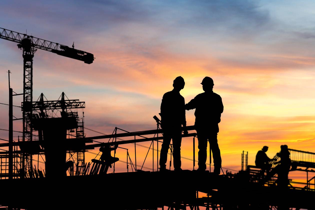 Construction workers silhouetted against a sunset at a building site.