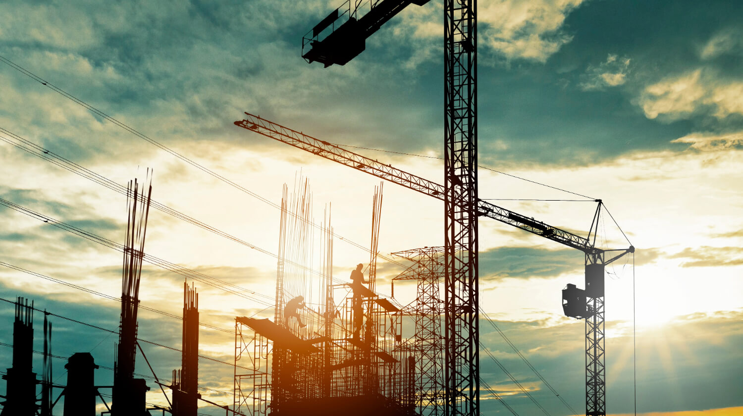Construction site silhouette with cranes and beams at sunset.
