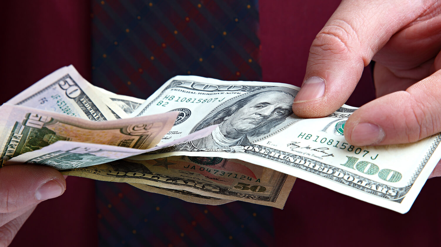 Hands exchanging various U.S. currency bills, representing commercial debt collection.