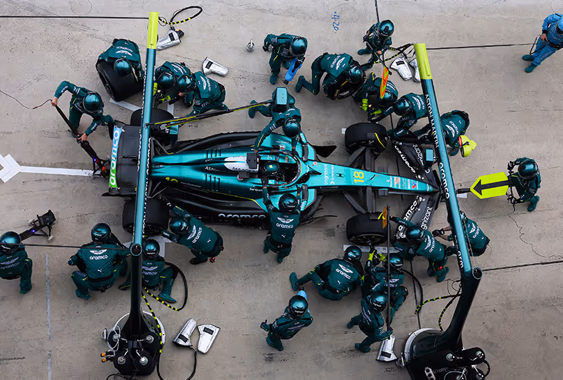Overhead view of the Aston Martin Aramco F1 pit crew surrounding the teal race car during a high-speed pit stop.