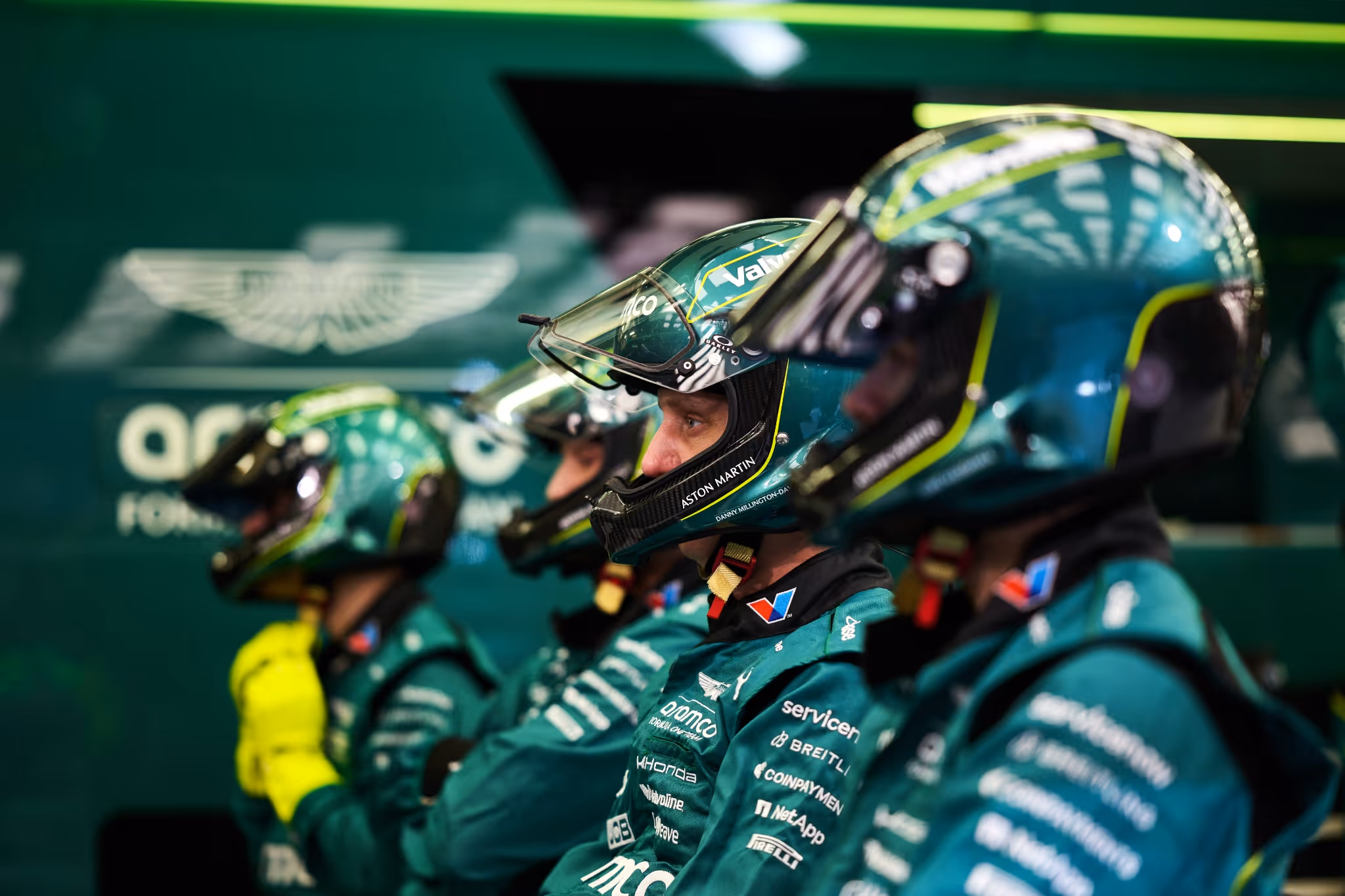 Racing crew members in green uniforms and helmets standing in a row.