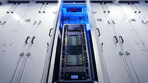 A GB300 server rack inside a white, enclosed data-center cabinet, with exposed servers, cooling fans, network components, and dense yellow and blue cabling illuminated by blue light.