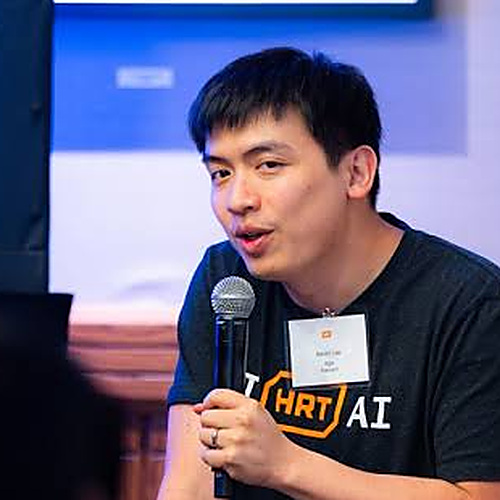 Kevin Lee speaking into a microphone wearing a black T-shirt with an orange HRT logo.