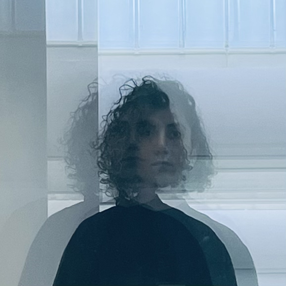nazanin oghanian with curly hair wearing dark clothing, photographed through layered glass panels, creating multiple overlapping reflections that produce a fragmented portrait effect.