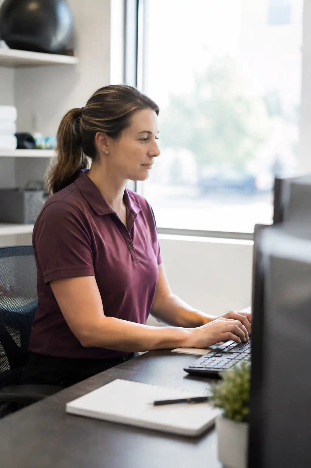 physical therapist in a purple shirt working on her laptop with the Stride EMR open in the browser