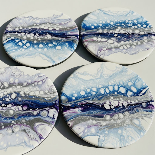 Four round coasters with abstract blue, white, black, and purple fluid art designs featuring bubble-like patterns.
