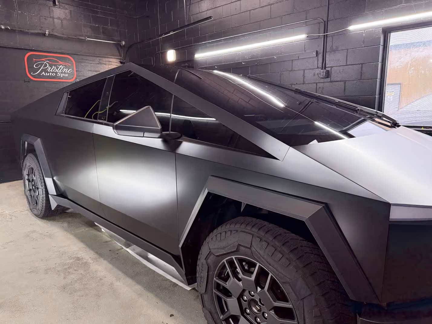 Side view of a matte black Tesla Cybertruck with tinted windows inside a garage.
