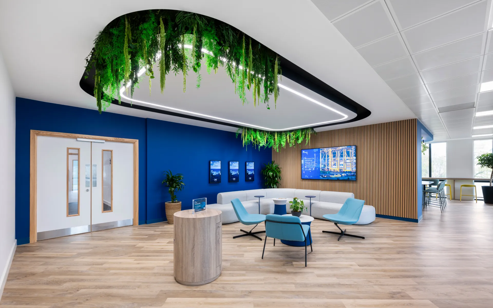 Modern breakout space designed for BMT featuring hanging green foliage, blue accent walls, and wood flooring.