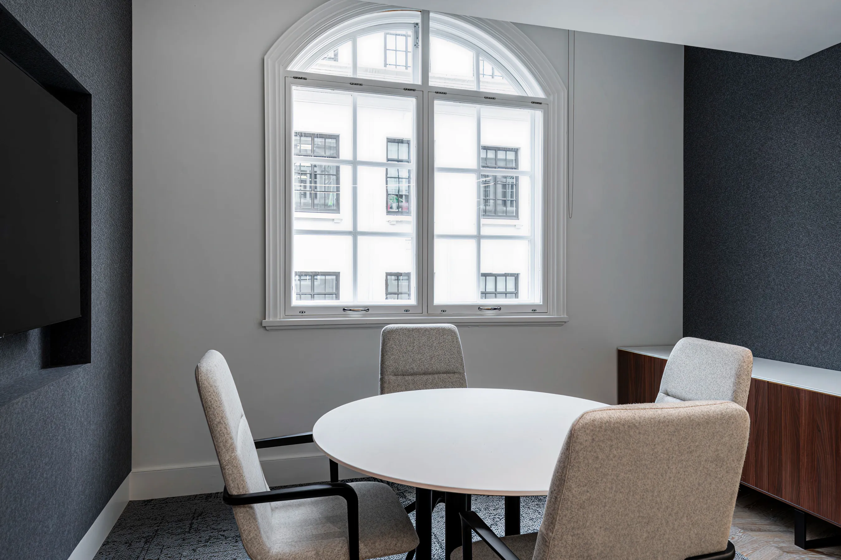 Small meeting area with a round table, cushioned chairs, and a large arched window letting in natural light.