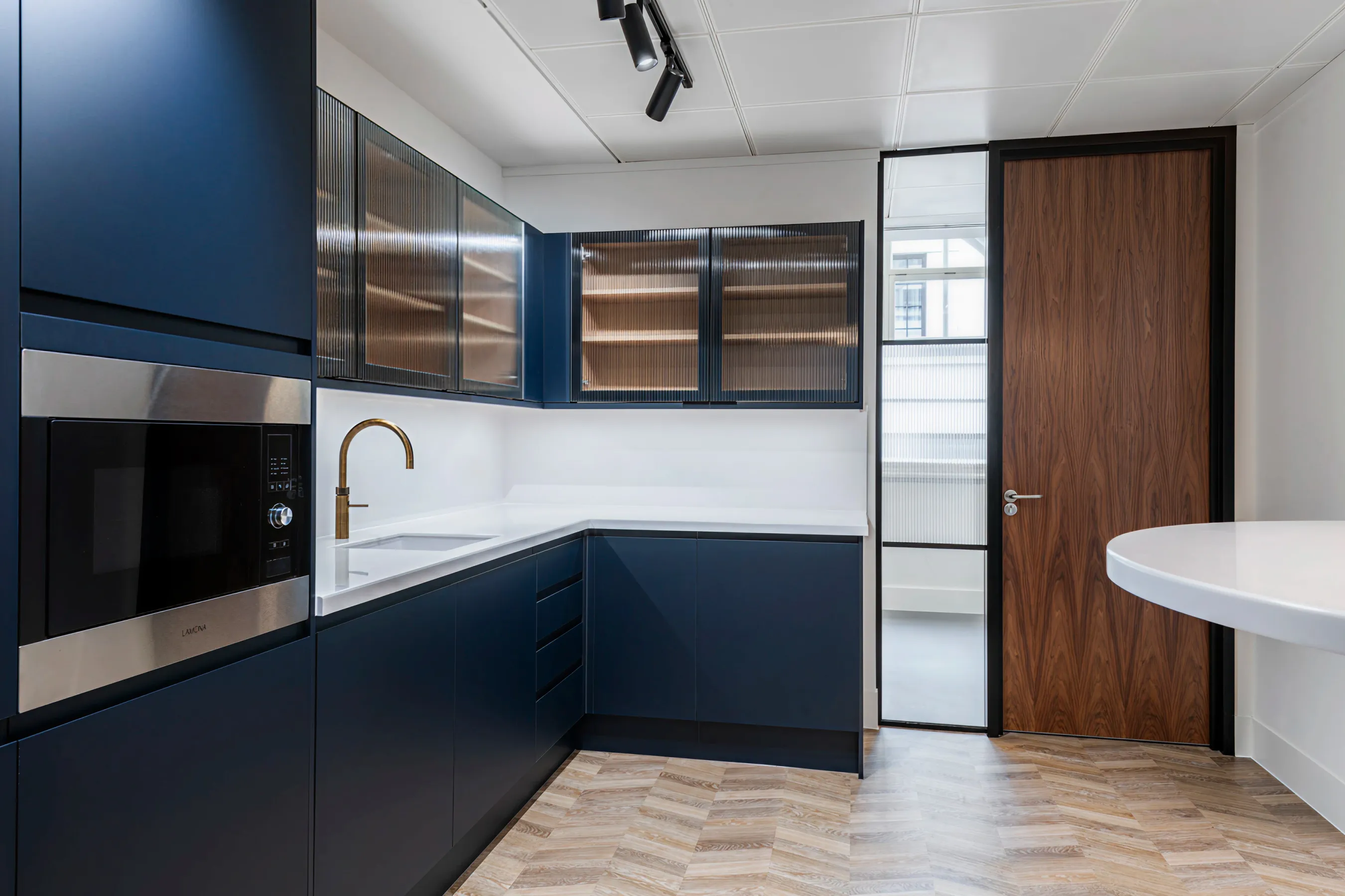 Sleek kitchenette area in an office, featuring dark blue cabinets, wood finishes, and integrated appliances.
