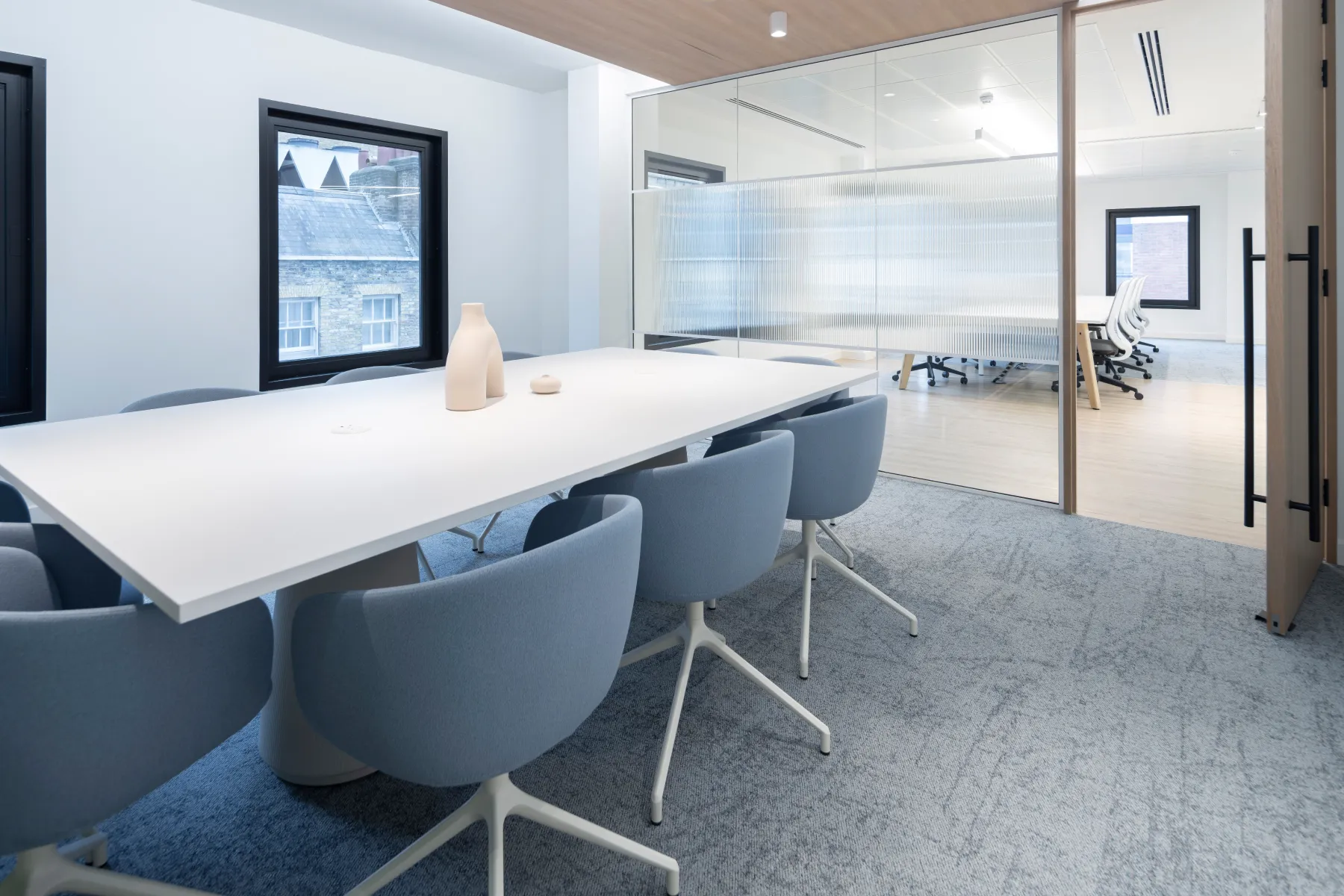 Bright meeting room with a long white conference table, blue chairs, and glass walls.