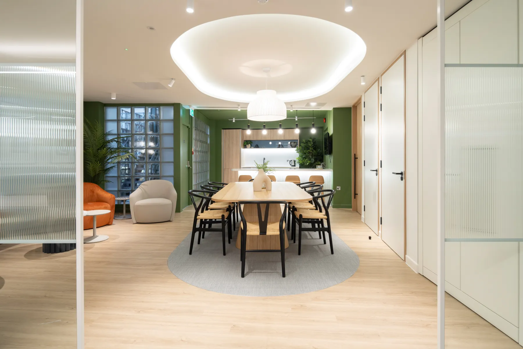 Glass-walled meeting room with a wooden table, modern chairs, and a large circular ceiling light.